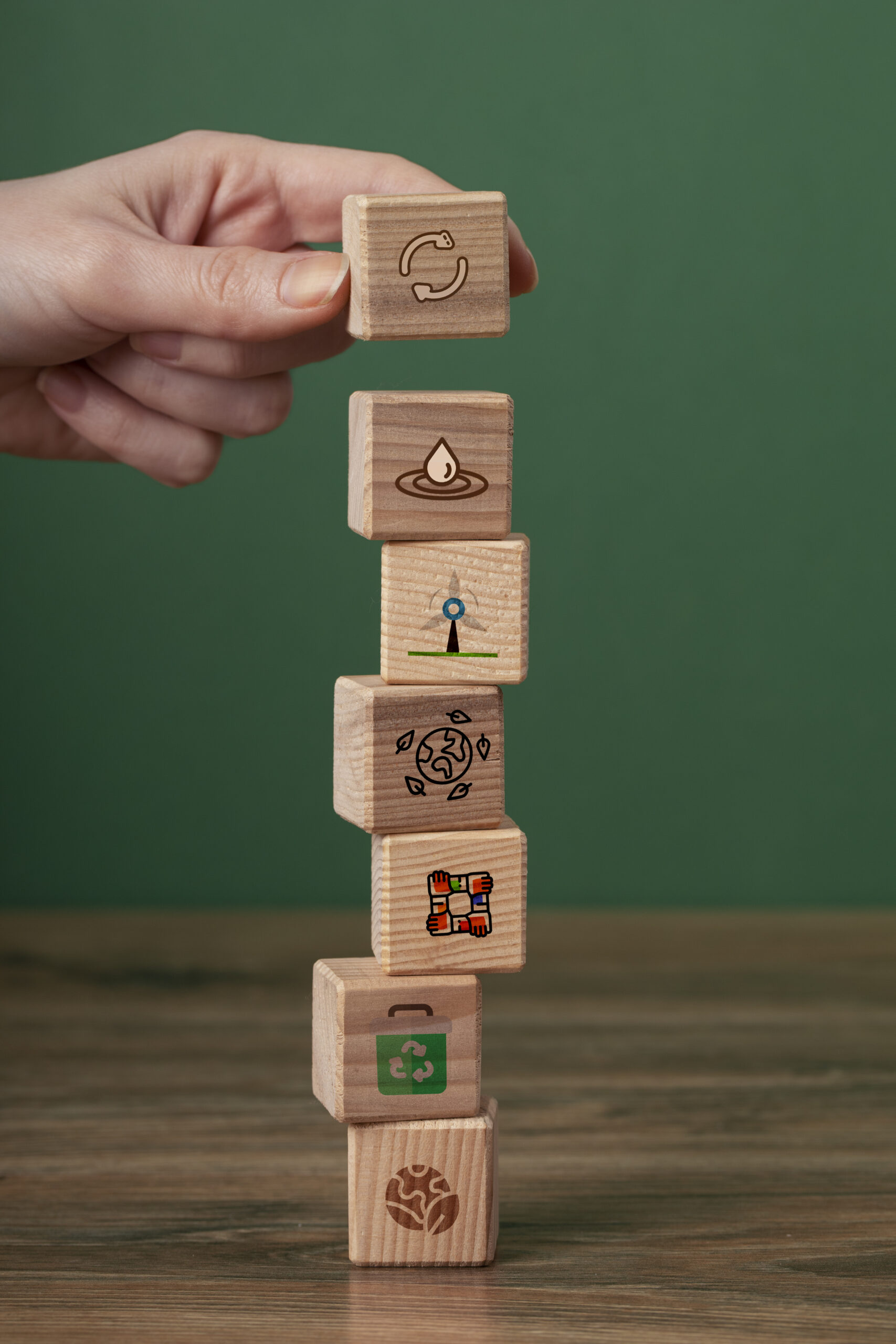Mão organizando blocos de madeira com ícones de sustentabilidade, reciclagem e preservação ambiental, representando os valores ecológicos da Gallo Pneus.